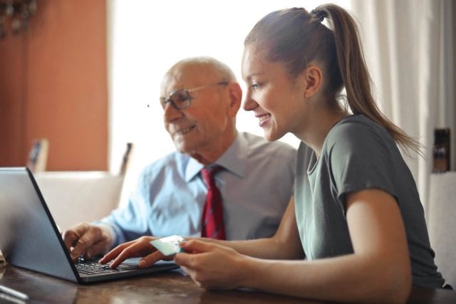A young woman works at a computer with an older adult next to her.