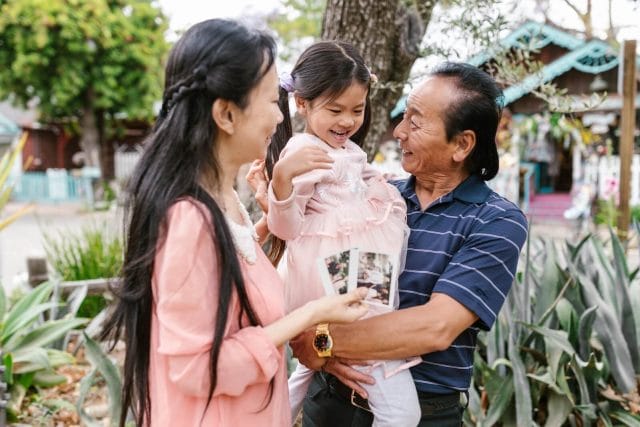 Woman looks at her father smiling while holding her child.
