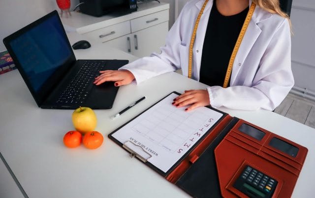 An overhead image of a dietitian working at her desk. She has a laptop computer, a meal plan scheduler, and healthy foods on her desk.