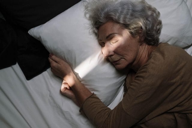 A senior woman sleeps in bed. A beam of light shines across her face.