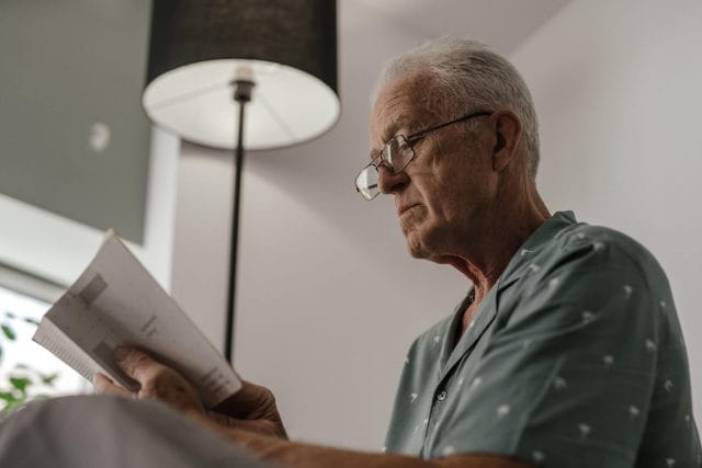 An older adult man wears glasses and reads a booklet.