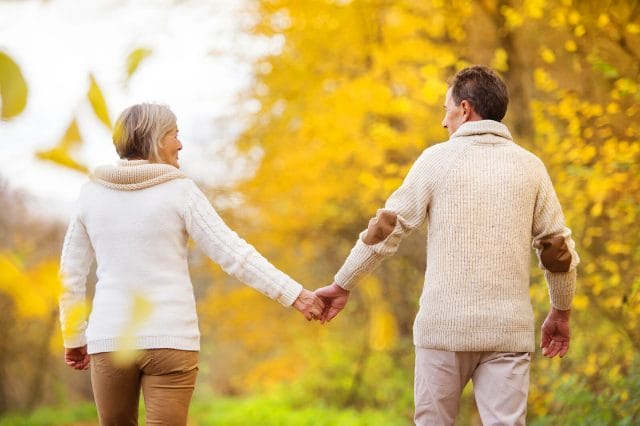 An image taken behind a couple walking outside on a cool fall day while holding hands.