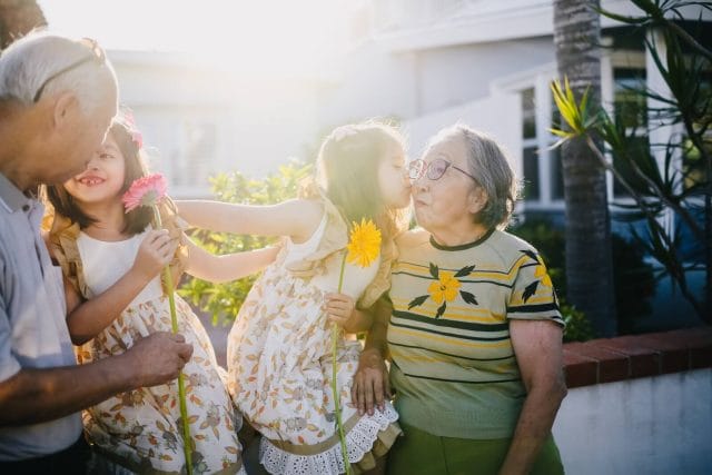 Two young children hold flowers and smile at their grandparents.