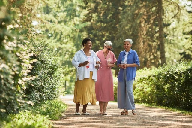 Three older adult women walk along an outdoor path together.