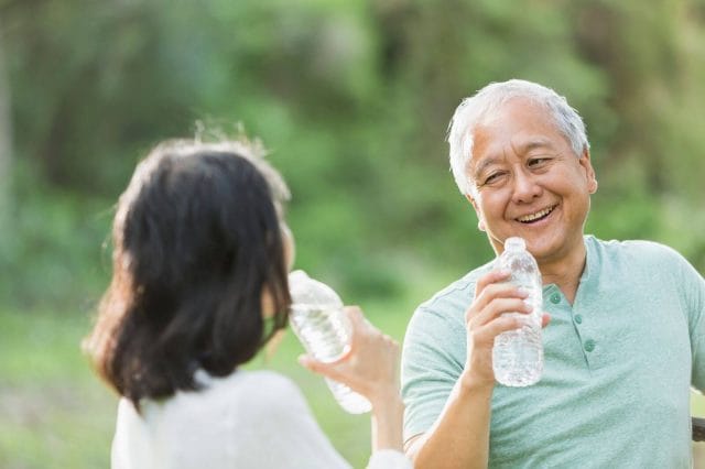 An older adult man and woman are outside drinking bottles of water.