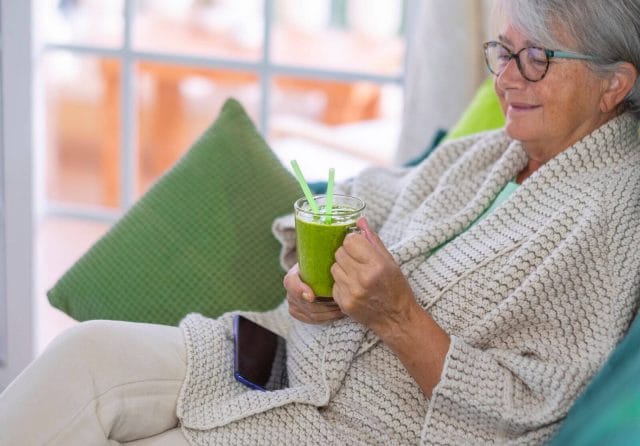 An older adult woman sits, holding a smoothie.